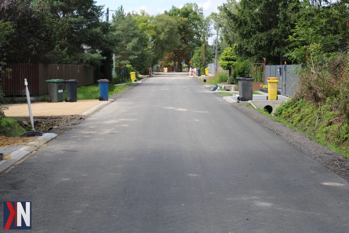 Zdjęcie przedstawia roboty budowlane w Łodzi, gdzie trwają prace utwardzania ulic gruntowych. Nowa nawierzchnia asfaltowa zostanie wprowadzona na 42 ulicach do końca roku, a do wakacji zakończy się etap modernizacji na 21 drogach. W tle widoczny pracujący sprzęt budowlany oraz ekipa robotników.