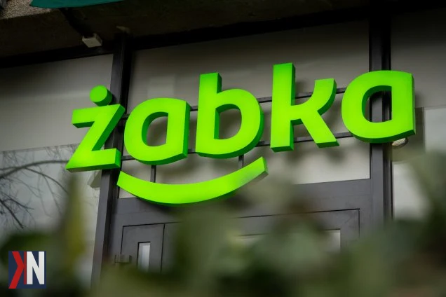 Zdjęcie przedstawia logo sieci sklepów Żabka, symbolizujące popularność marki w polskich miastach i na osiedlach. Artykuł omawia plany właściciela Circle K dotyczące przejęcia Żabki, znanej jako punkt codziennych zakupów oraz miejsce odbioru przesyłek i zakupu kawy.