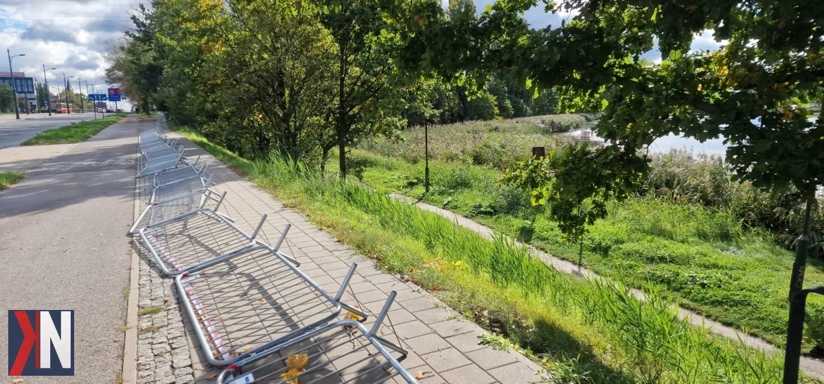 Zdjęcie przedstawia staw na Księżym Młynie w Łodzi, otoczony zielenią, w kontekście planowanych inwestycji deweloperskich oraz zagospodarowania przestrzeni publicznej. Artykuł informuje o zbliżających się szczegółach dotyczących przyszłości stawu, co budzi zainteresowanie mieszkańców okolicy.