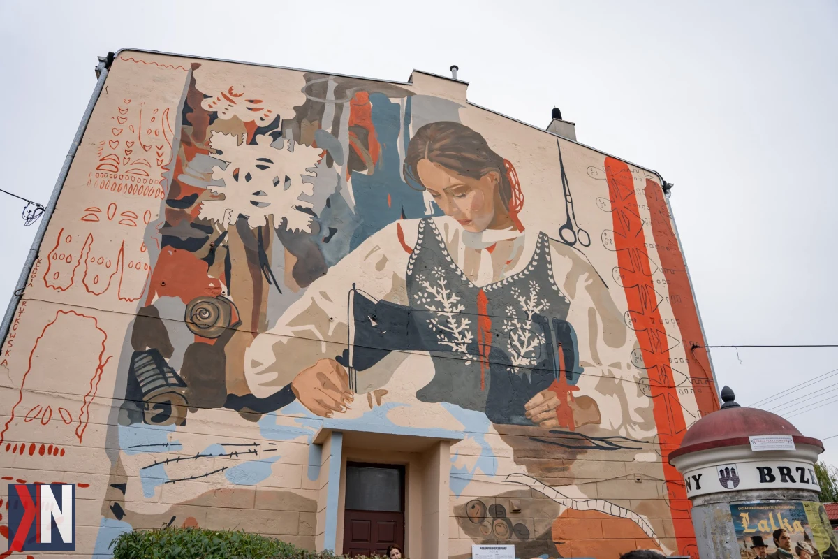 Zbliżenie na mural w Brzezinach przedstawiający historię miasta krawców, z kolorowymi wzorami i artystycznymi detalami, które ożywiają lokalną tradycję. Dzięki nowoczesnej technologii wystarczy smartfon, aby odkrywać fascynujące opowieści związane z przeszłością tego urokliwego miejsca.