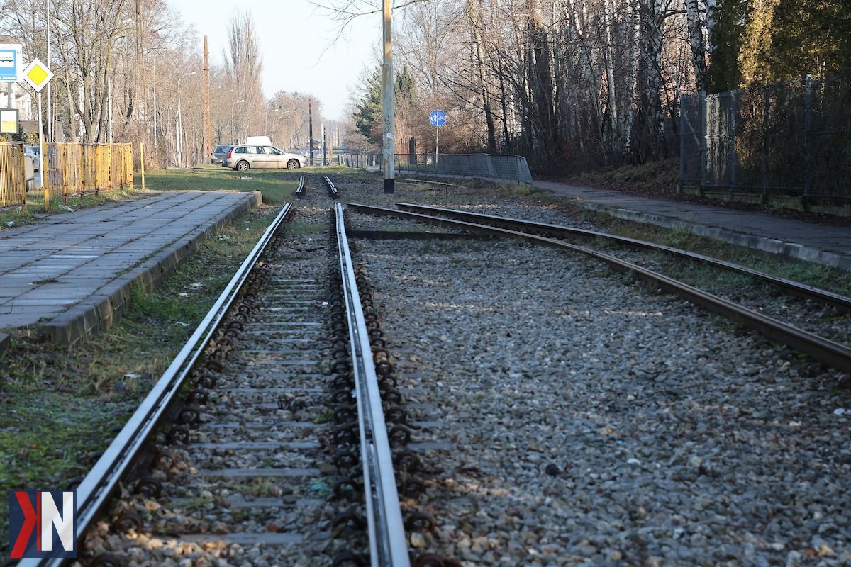 "Tramwaj na ulicy Warszawskiej w Łodzi - widok na trasę, która zostanie odnowiona w ramach remontu. Oczekiwanie na powrót linii tramwajowej 'trójki' na Marysin i Rogi. W tle nowoczesne maszyny budowlane oraz zieleń otaczająca trasę, symbolizująca rozwój komunikacji miejskiej w Łodzi."
