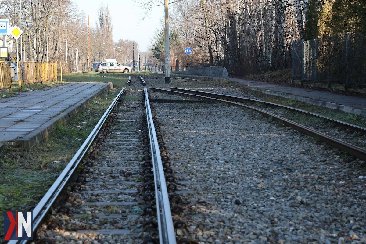 "Tramwaj na ulicy Warszawskiej w Łodzi - widok na trasę, która zostanie odnowiona w ramach remontu. Oczekiwanie na powrót linii tramwajowej 'trójki' na Marysin i Rogi. W tle nowoczesne maszyny budowlane oraz zieleń otaczająca trasę, symbolizująca rozwój komunikacji miejskiej w Łodzi."