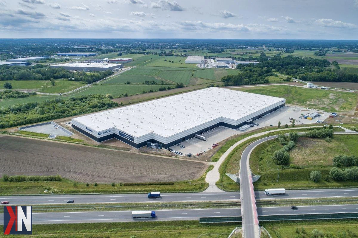 Zdjęcie przedstawia budowę nowej hali logistycznej firmy Hillwood w Chlebni pod Grodziskiem Mazowieckim. W tle widoczny jest rozwijający się park logistyczny, który zyska ponad 36 tys. mkw. powierzchni magazynowej i biurowej, przyciągając inwestorów i wspierając rozwój regionu.