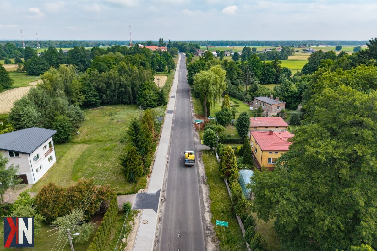 "Modernizacja drogi wojewódzkiej nr 485 w Drużbicach - prace remontowe trwają, poprawiając infrastrukturę w województwie łódzkim. W tle zdjęcia widać sprzęt budowlany oraz ekipy robocze zaangażowane w projekt."