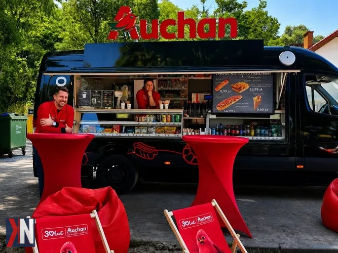 Zdjęcie przedstawia mobilny food truck Auchan w Łodzi, który oferuje świeże jedzenie i napoje, symbolizując nową strategię hipermarketów, które dostosowują się do potrzeb klientów. W artykule omawiamy, jak Auchan wychodzi naprzeciw oczekiwaniom lokalnych społeczności.