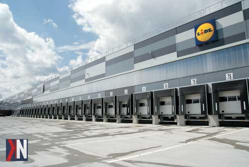 "Budowa nowego centrum logistycznego Lidla w gminie Buczek, Łódzkie – inwestycja stworzona z myślą o rozwoju lokalnej gospodarki i utworzeniu ponad 250 miejsc pracy. Zdjęcie przedstawia widok terenów budowy oraz przyszłego obiektu logistycznego."